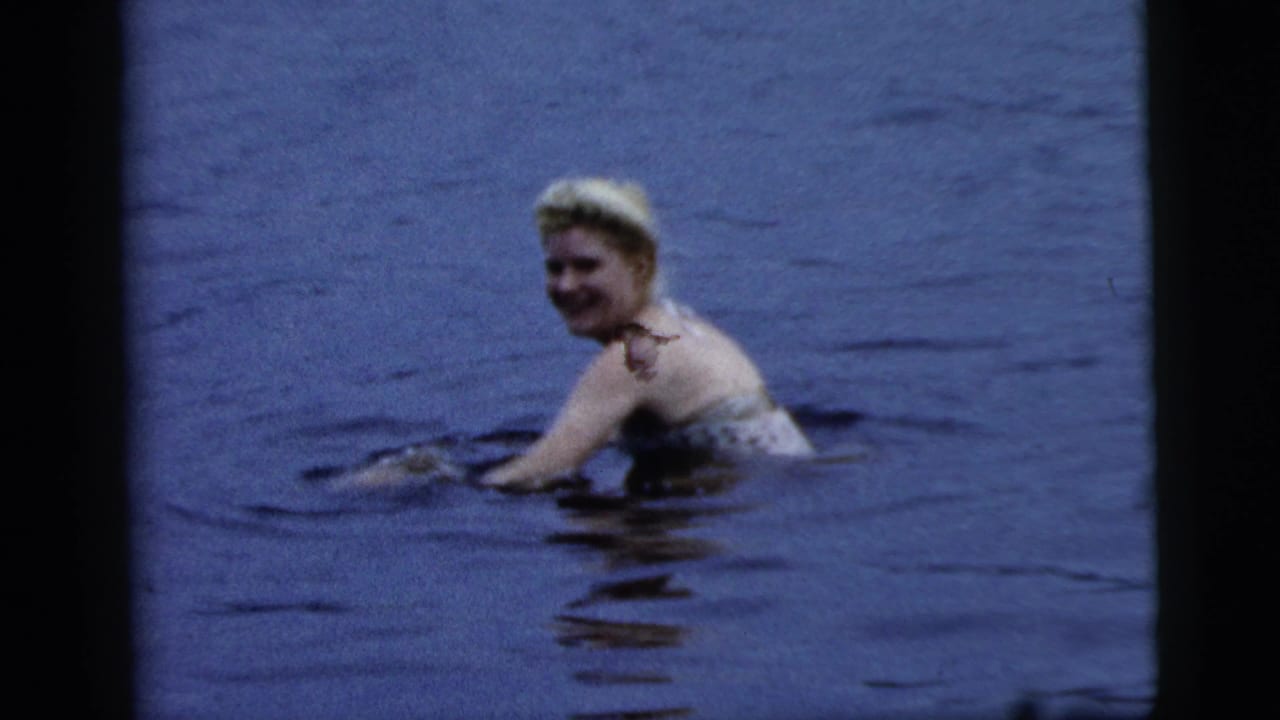 Blonde woman smiles while swimming in blue lake water.