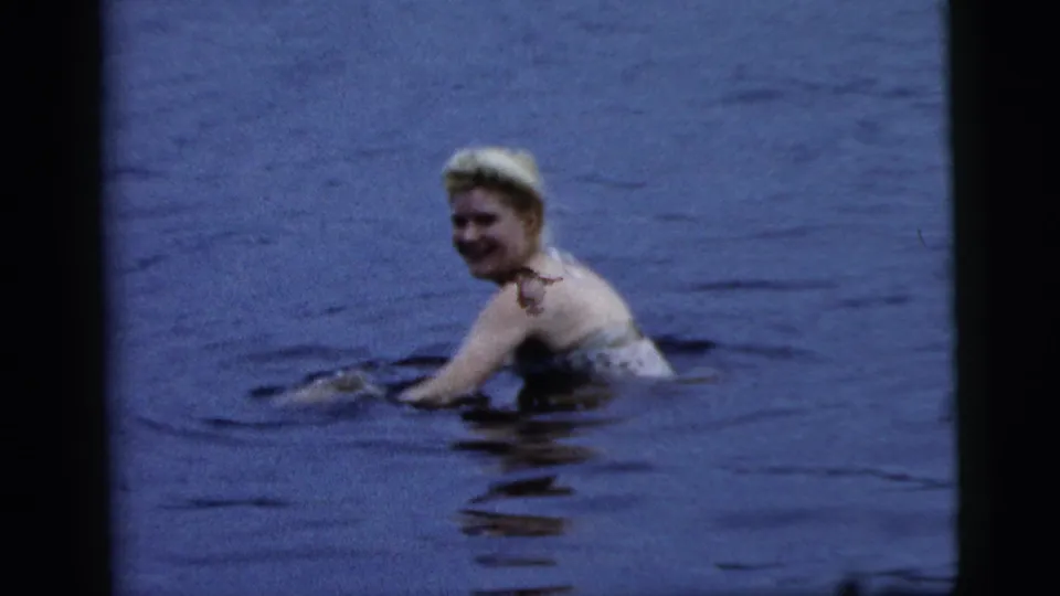 A blonde woman smiles toward the camera while swimming in a lake in metadata-identified Camden, New Jersey, 1961 footage.