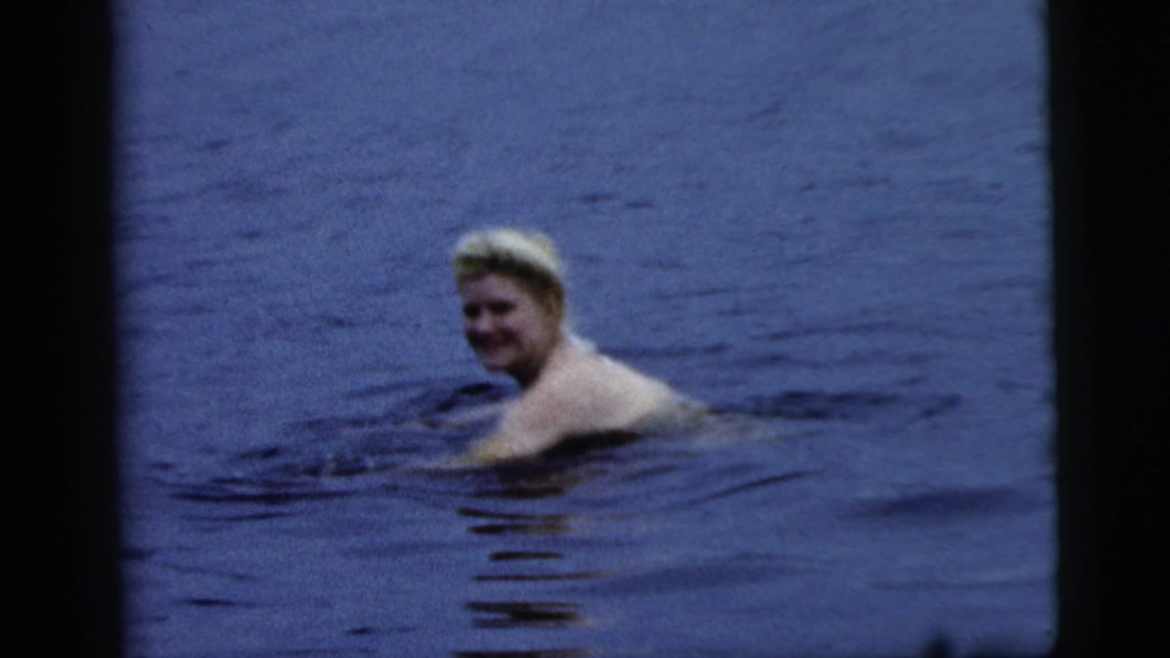 Blonde woman swims through open blue water and looks toward the camera.