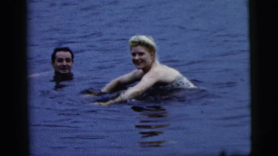 A woman and a man are visible together in the lake, both partly submerged and facing the camera in the 1961 Camden footage.
