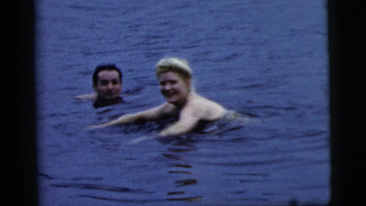 Two adults swim in open lake water, with the woman smiling toward the camera.