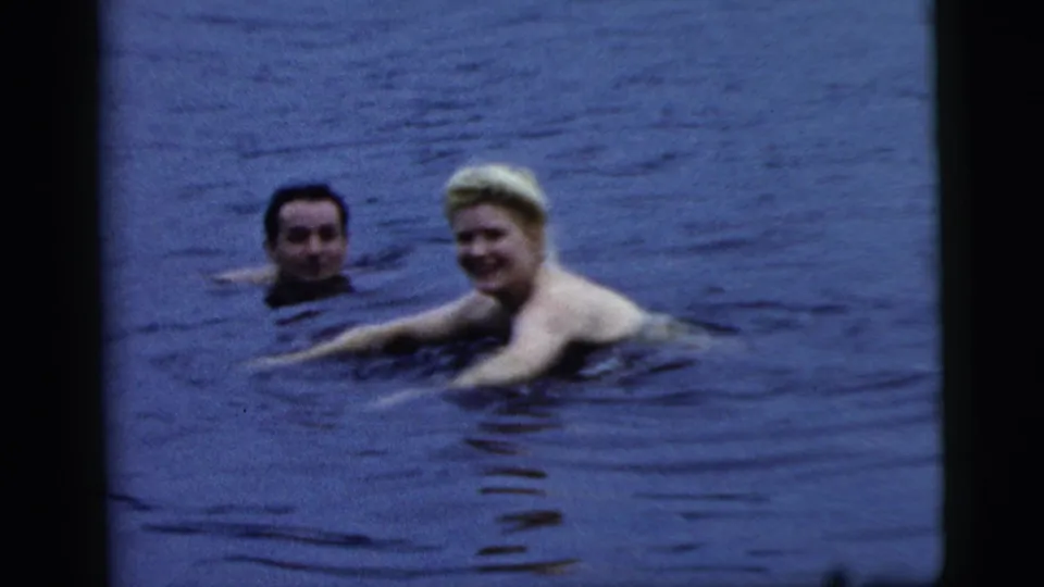 1961 Camden, New Jersey home-movie frame of two adults swimming in a lake, the woman smiling while the man floats nearby.