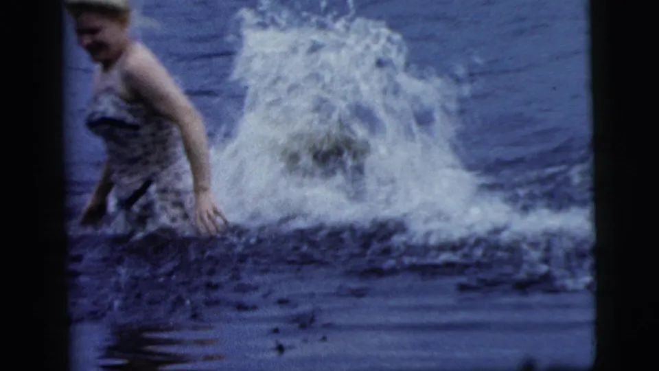 1961 Camden, New Jersey home-movie frame of a woman in lake water as a large splash rises behind her.