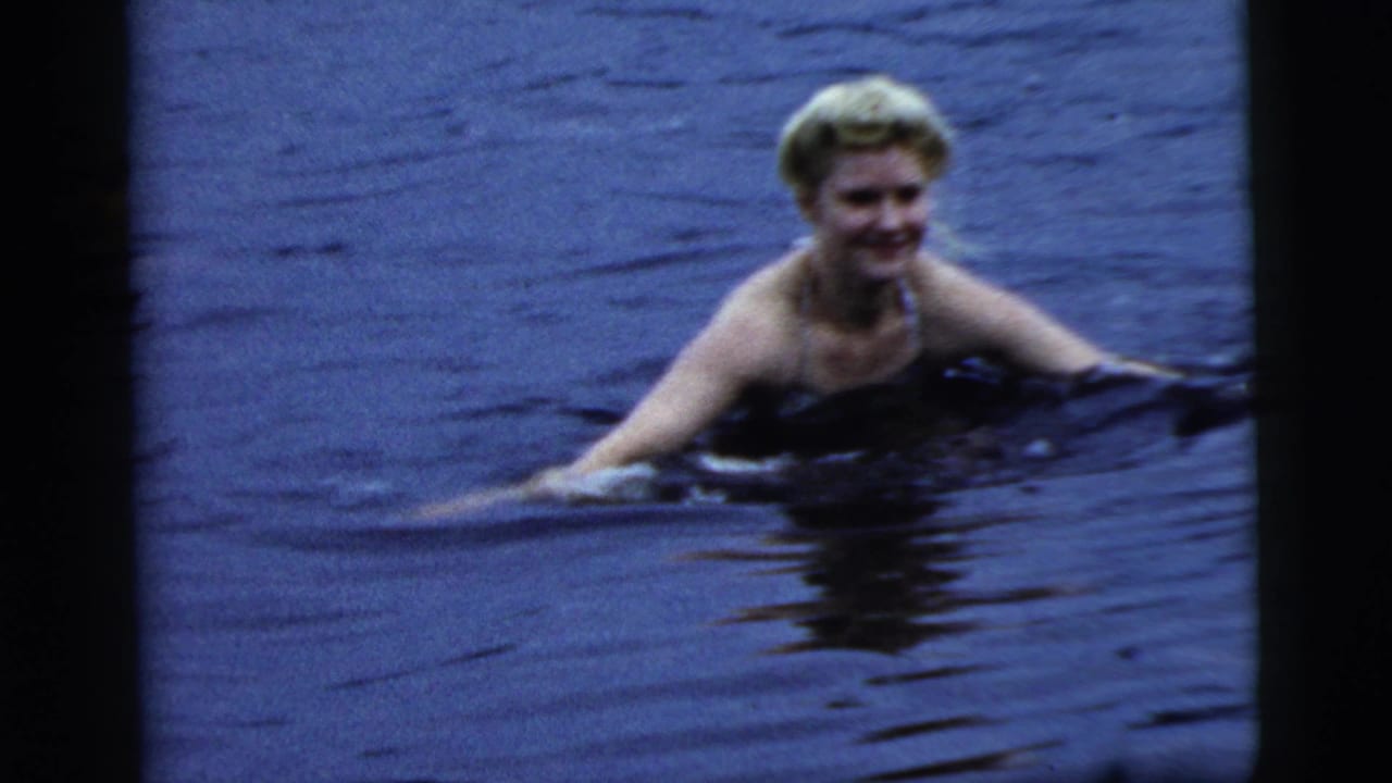 A blonde woman smiles while wading in dark water, with her shoulders above the surface.
