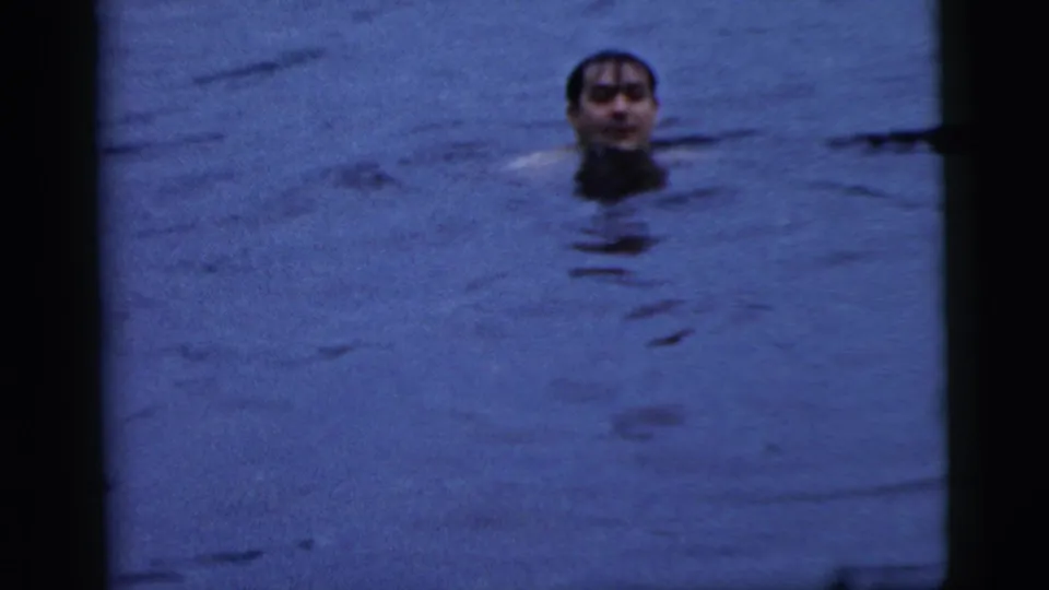 1961 Camden home-movie frame of a brunet man treading in dark water, seen from the shoulders up.