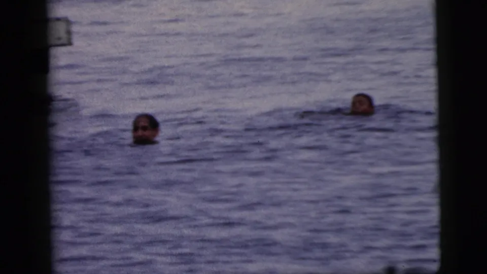 1961 Camden waterfront frame with two swimmers moving through open water, partially obscured by soft focus and film borders.