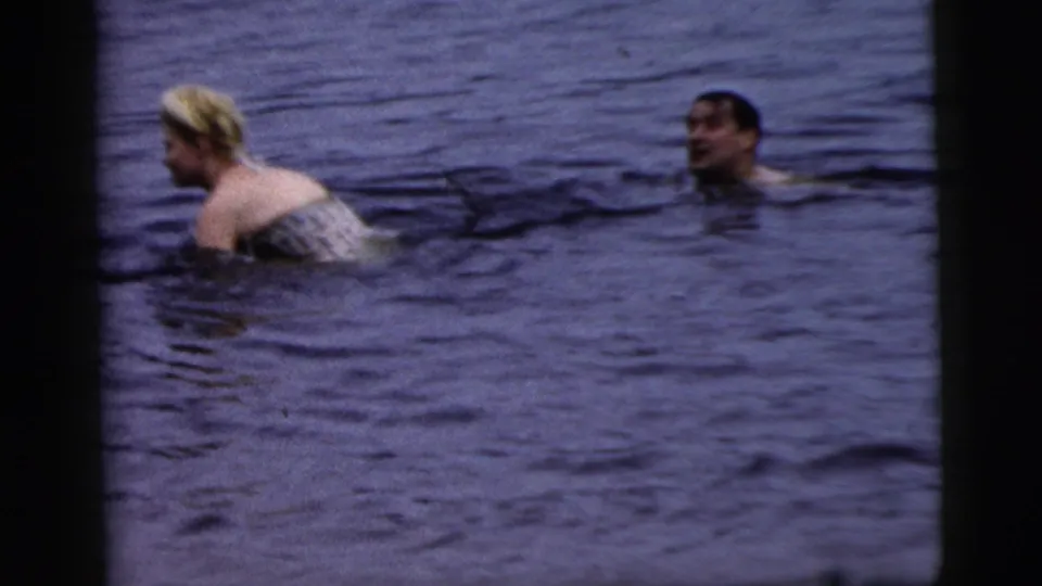 A woman in light swimwear and a second swimmer appear in open water in 1961 Camden, New Jersey 8mm footage.