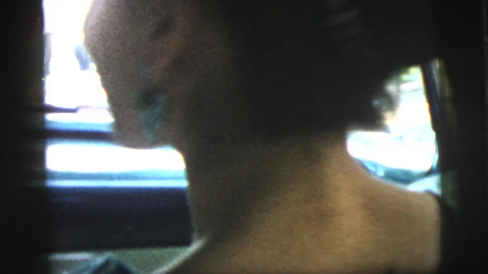 1961 Camden car-interior frame with the woman turned partly toward the camera, her face softly visible against bright window light.