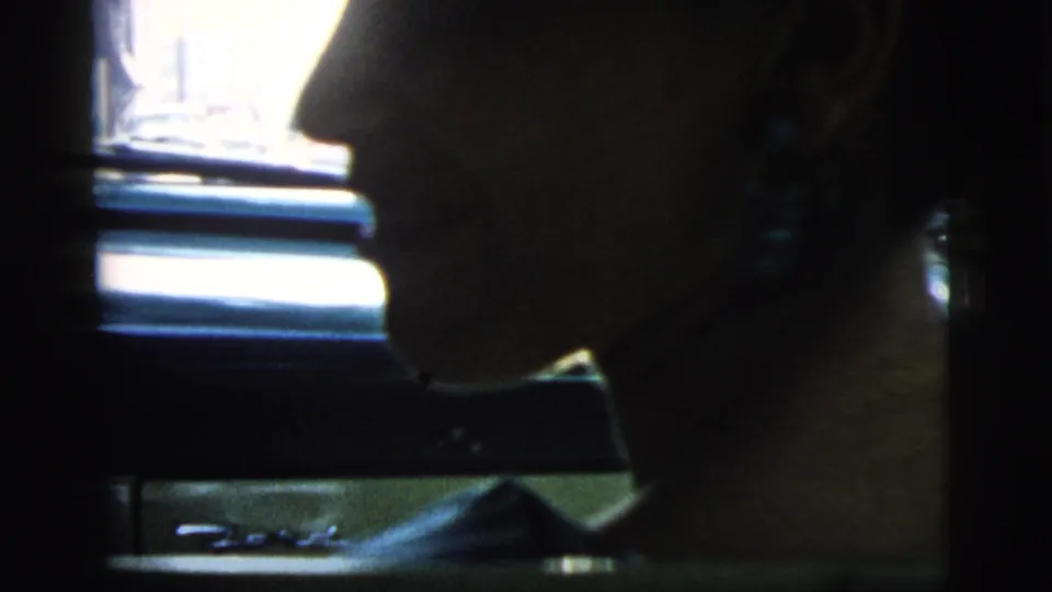 Close 8mm frame of the woman in profile inside the car, with dangling earrings visible and window light outlining her face.