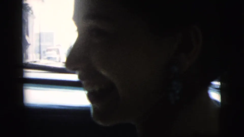 In 1961 Camden, New Jersey footage, a woman sits in profile inside a car, partly silhouetted against the bright window.