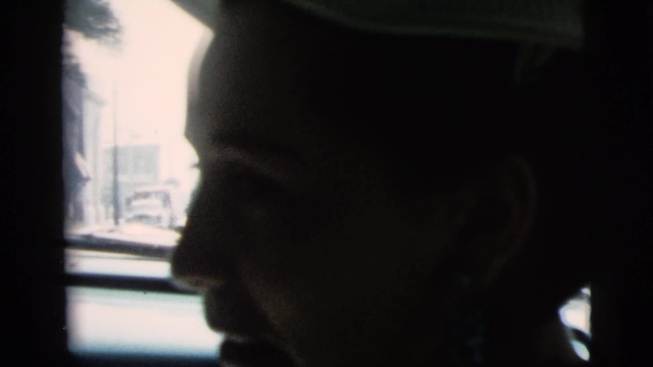 Close side profile of a woman wearing a light hat and blue-green earrings in a car.