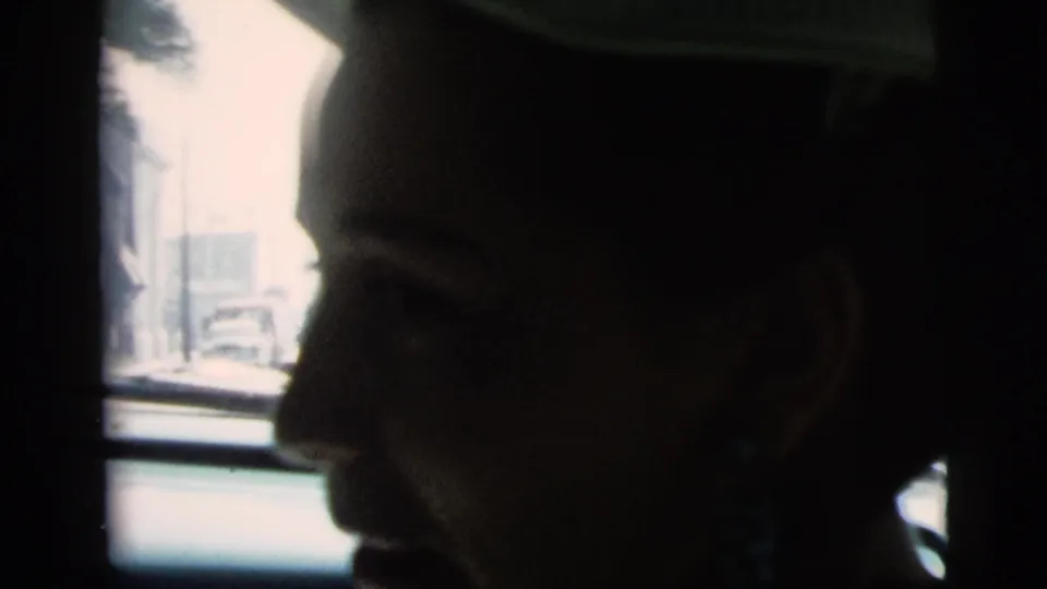 The woman appears in close profile inside the car, wearing a light-colored hat and dangling blue-green earrings.