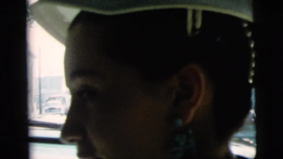 A clearer profile shows the woman smiling slightly inside the car, with her hat brim and turquoise-toned earrings visible.