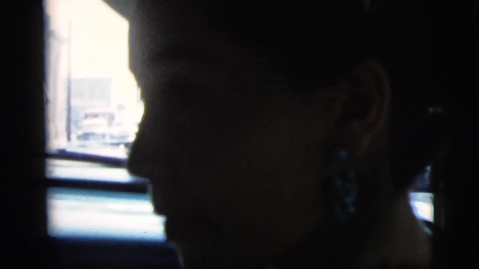 The final frame holds on the woman's shadowed profile in the car, with the sunlit street outside visible through the window.