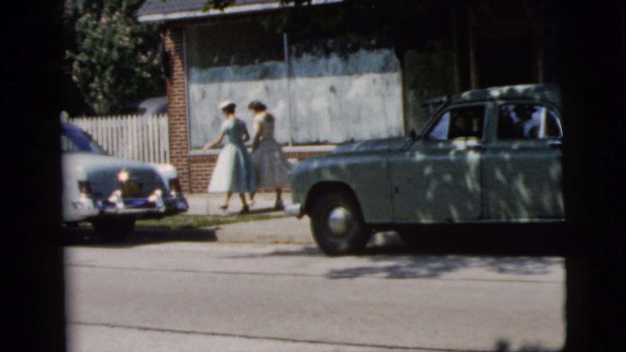In Camden, New Jersey wedding footage from 1961, two women in full-skirted dresses walk past early 1960s cars on a neighborhood sidewalk.