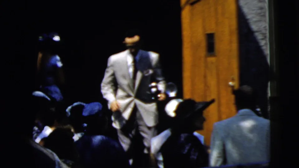 Suited guests and women in hats gather near wooden doors during the 1961 Camden wedding home movie sequence.