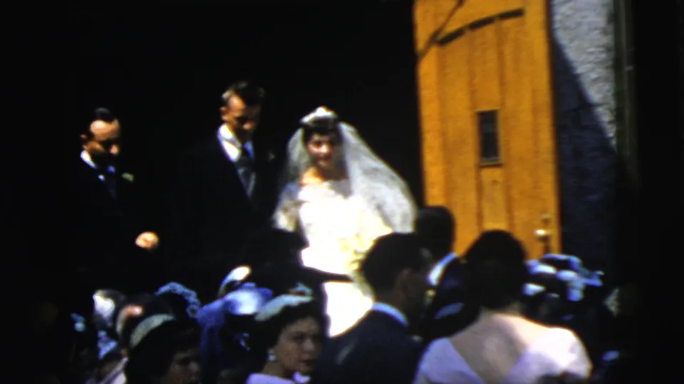 The bride in a white gown and veil stands beside the groom in a dark suit during the 1961 Camden church exit.