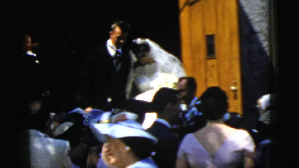 The 1961 Camden wedding couple remains near the wooden church door while guests in hats and suits crowd the foreground.