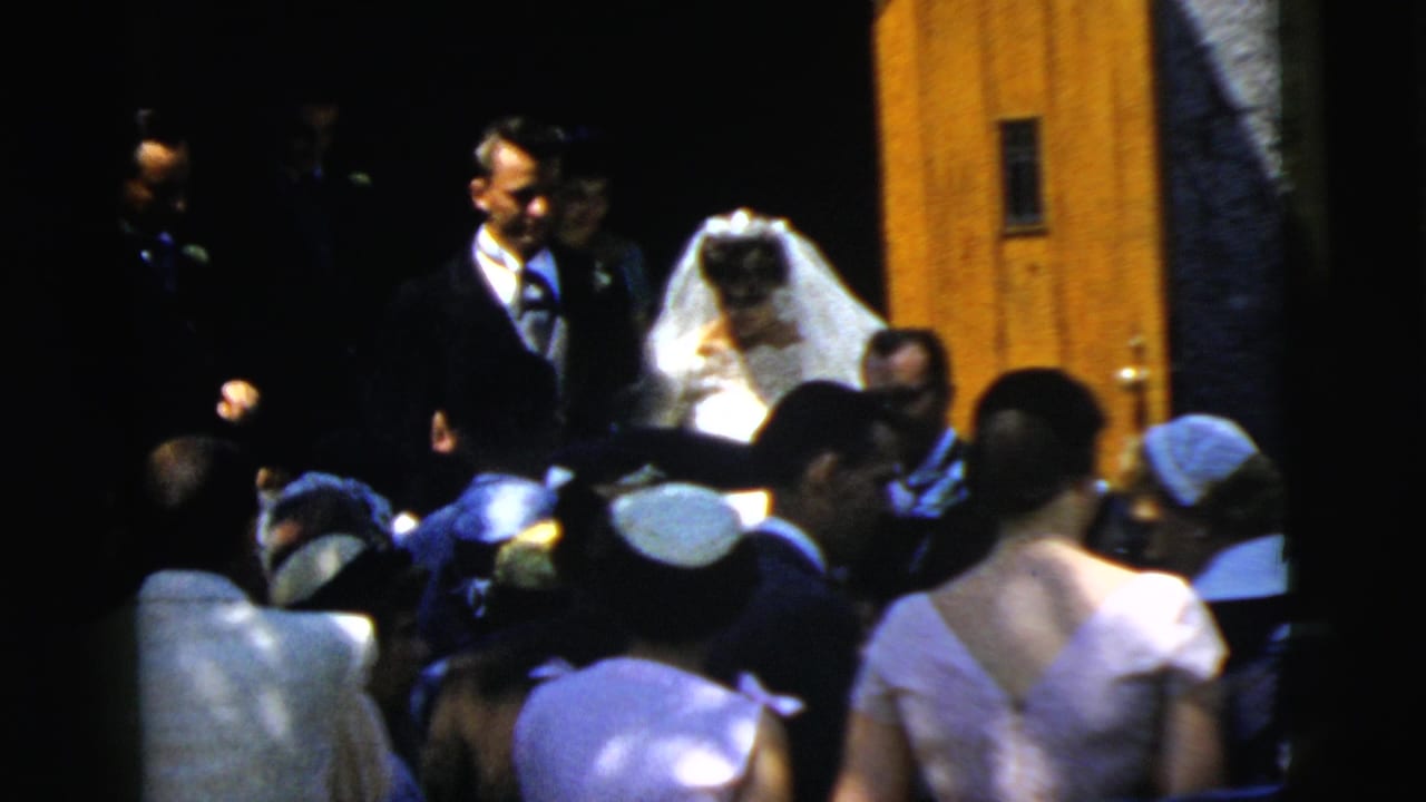 In Camden, New Jersey in 1961, a bride in a veil and groom in a dark suit leave a church doorway before a gathered crowd.