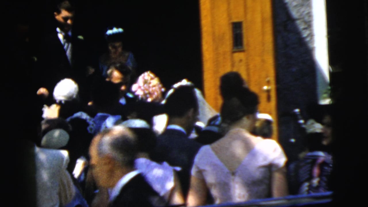 The 1961 Camden wedding party is partially visible at the church entrance, surrounded by guests in formal hats and dresses.