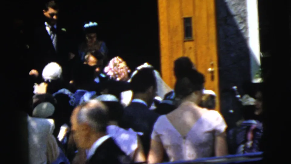 The 1961 Camden wedding party is partially visible at the church entrance, surrounded by guests in formal hats and dresses.
