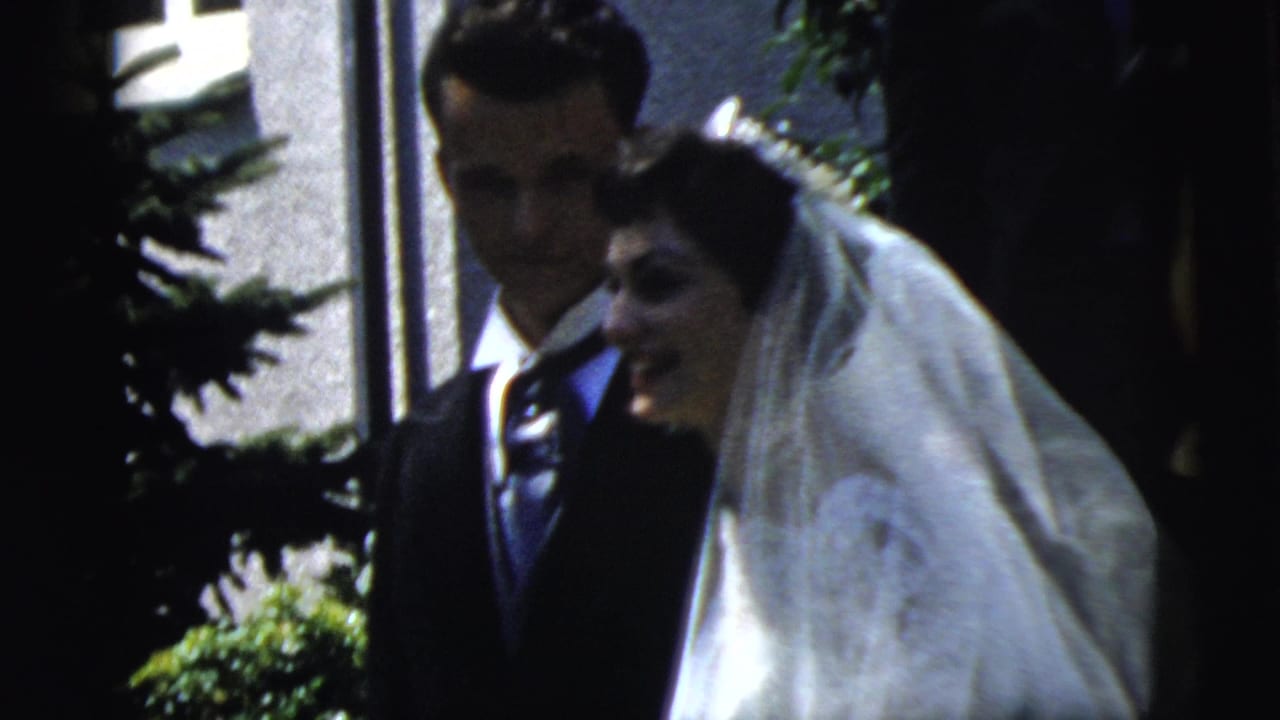 The bride and groom stand close together outside in Camden, New Jersey, with the bride smiling beneath her veil as foliage frames the shot.