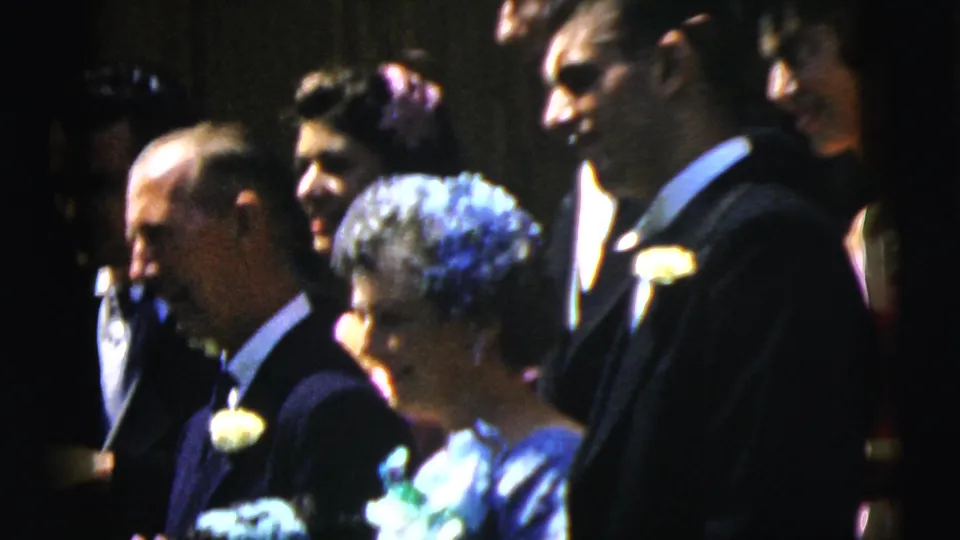 A group of Camden wedding guests stands outdoors in formal attire, including men in dark suits and women in dresses with floral accessories.