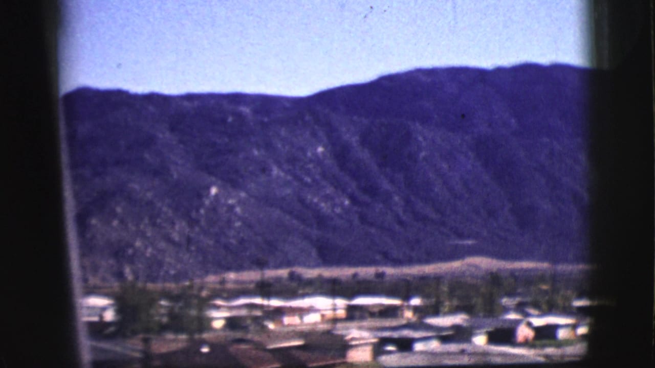 Distant mountain ridge and small town rooftops seen through dark window edges.