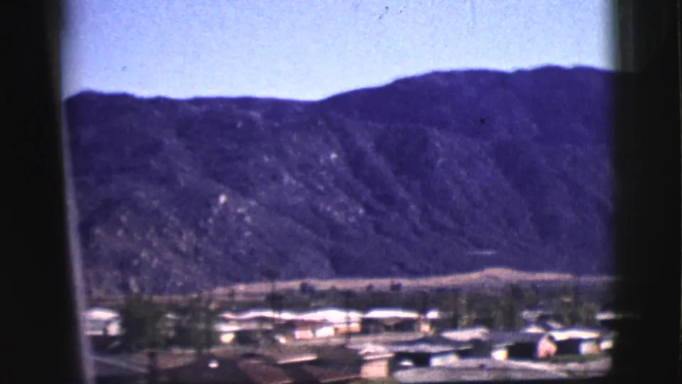 1961 Clarkdale, Arizona view of low buildings at the base of a purple-toned mountain ridge, framed by dark window edges.