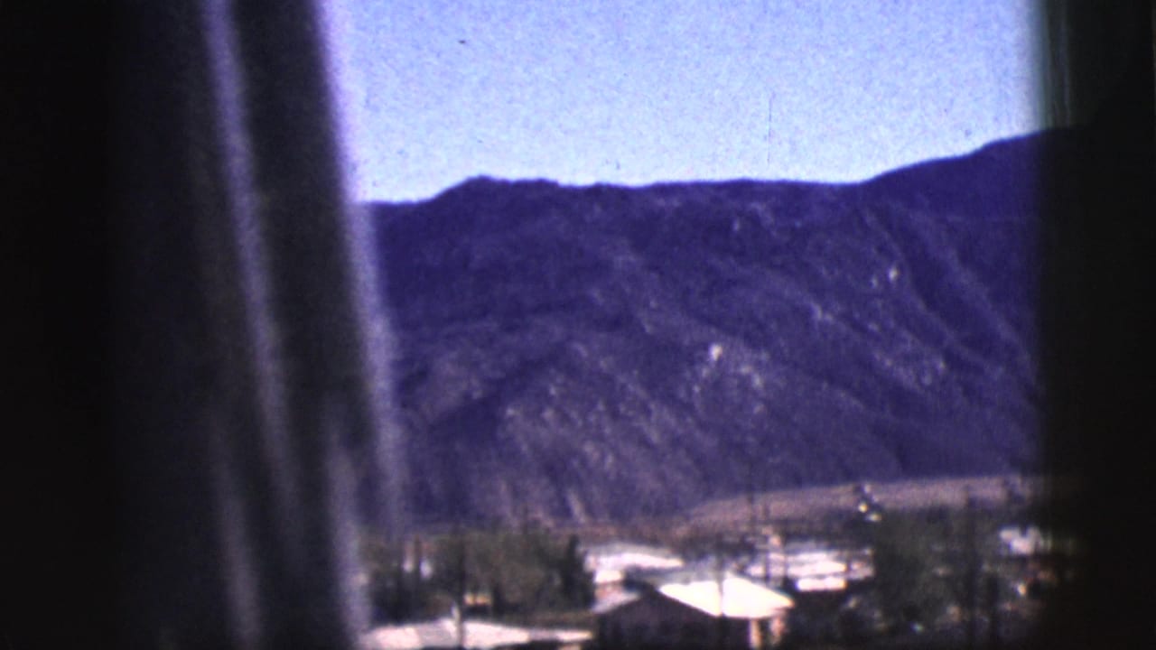 Clarkdale, Arizona town buildings and desert mountains appear beyond dark vertical window framing in this 1961 8mm frame.