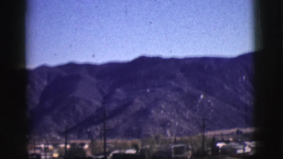 A rugged mountain ridge rises behind Clarkdale rooftops, trees, and utility poles in a soft 1961 8mm home-movie view.