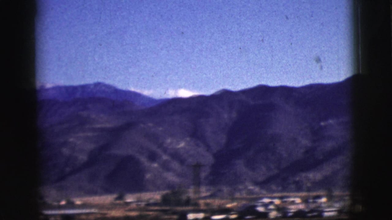 Mountain ridge under blue sky seen through dark vehicle window framing.