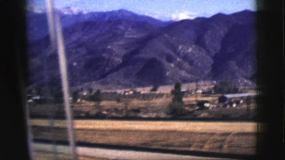 Moving-vehicle view of fields, small structures, and mountain ridges near Clarkdale, Arizona, from 1961 8mm footage.