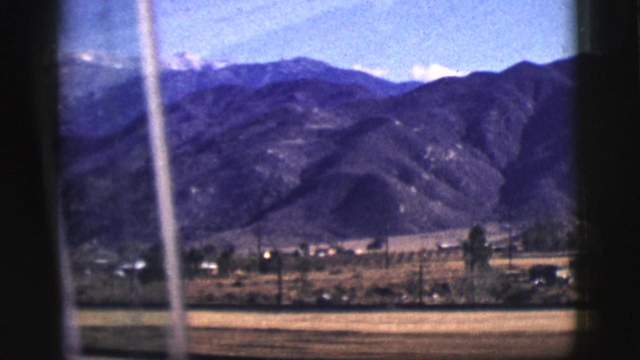 Mountain range seen through a vehicle window with valley buildings below.
