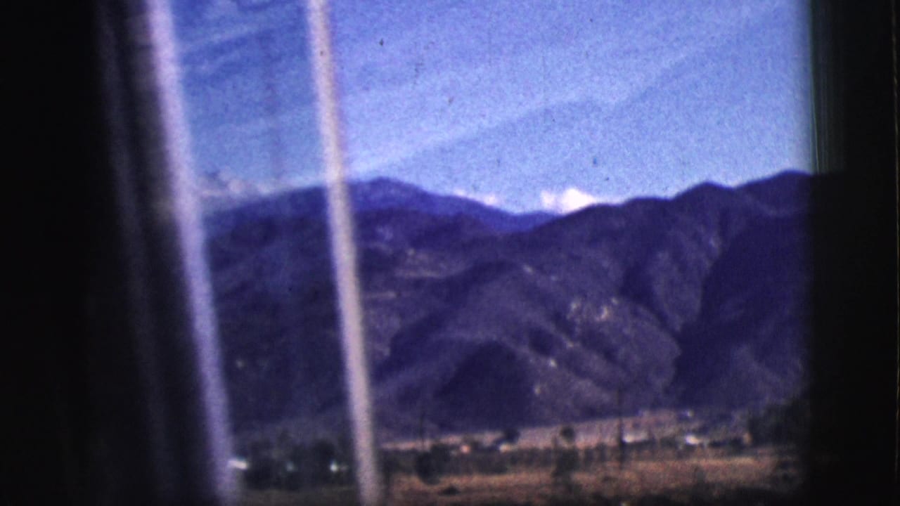 Dark window frame borders a distant mountain range and valley.