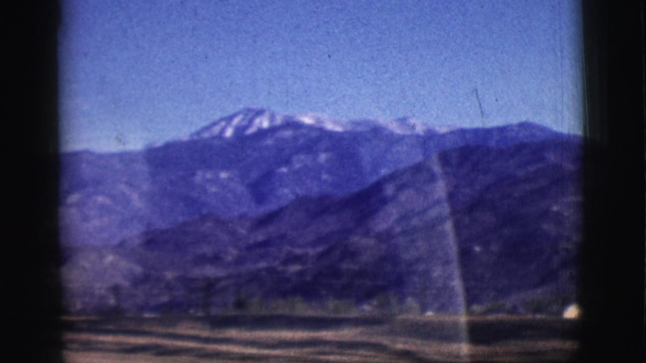 1961 Clarkdale, Arizona home-movie frame showing dark mountains, patches of snow, open ground, and window-edge shadows.