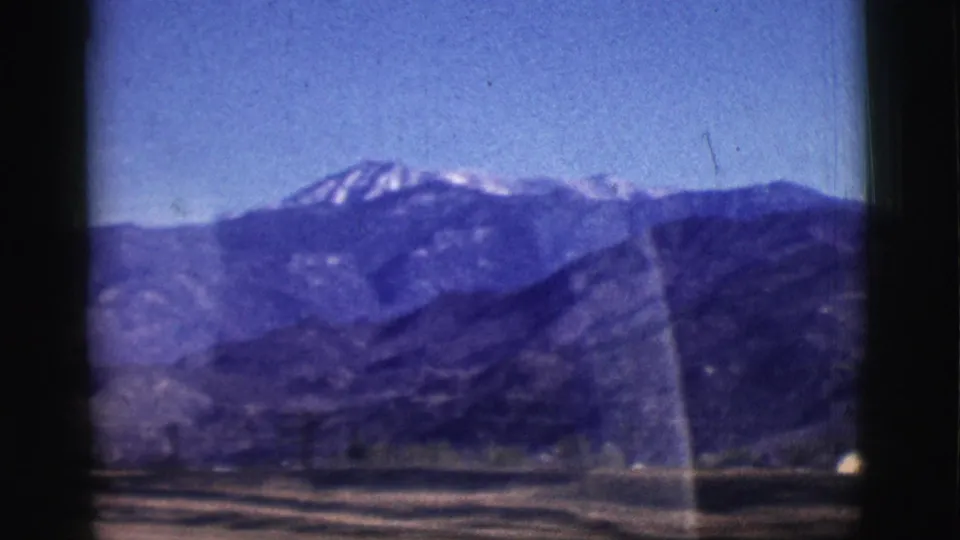 1961 Clarkdale, Arizona home-movie frame showing dark mountains, patches of snow, open ground, and window-edge shadows.