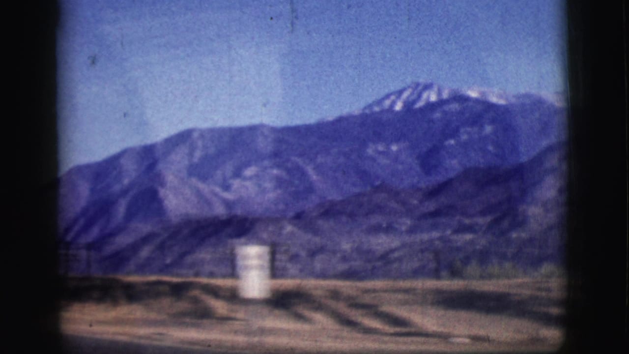 1961 Clarkdale, Arizona road view with snow-streaked mountains, open land, and a white cylindrical roadside marker.