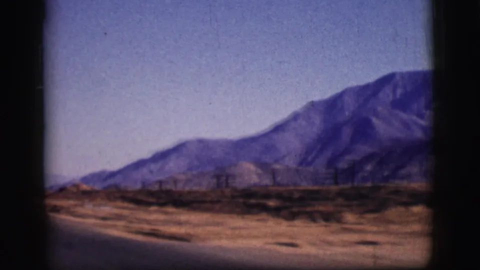1961 Clarkdale, Arizona home-movie view of a road edge, low desert terrain, utility lines, and a large mountain slope.