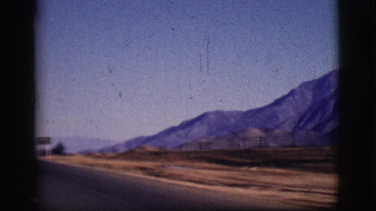 Paved road beside dry terrain with distant mountains under a pale sky.