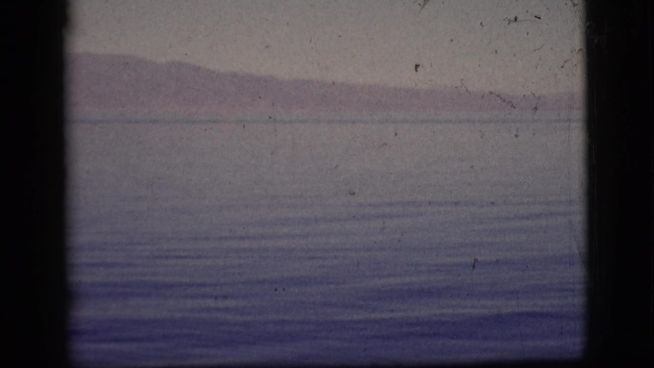 Distant mountains above a calm body of water with faint ripples and dark film gate edges.