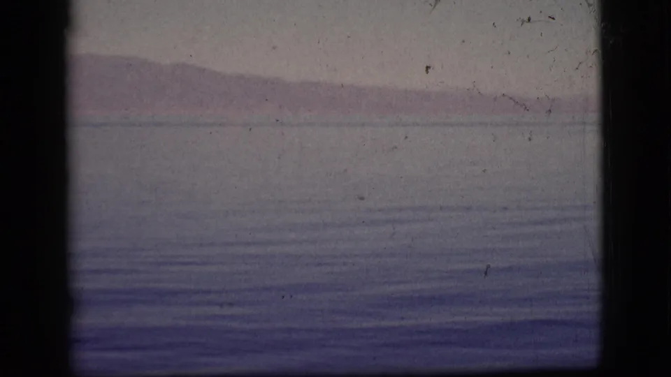 1961 8mm frame from Clarkdale, Arizona metadata showing hazy mountain ridges across calm water with visible film border and dust.