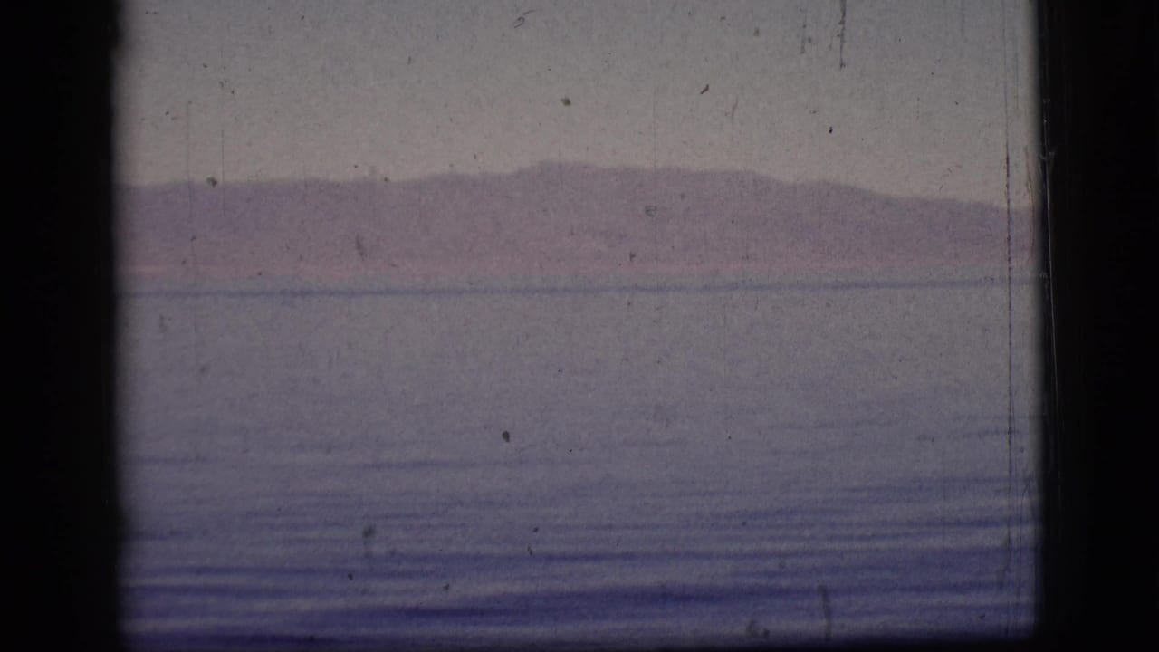 Calm water and distant low mountains seen through a dark vertical film gate shadow.