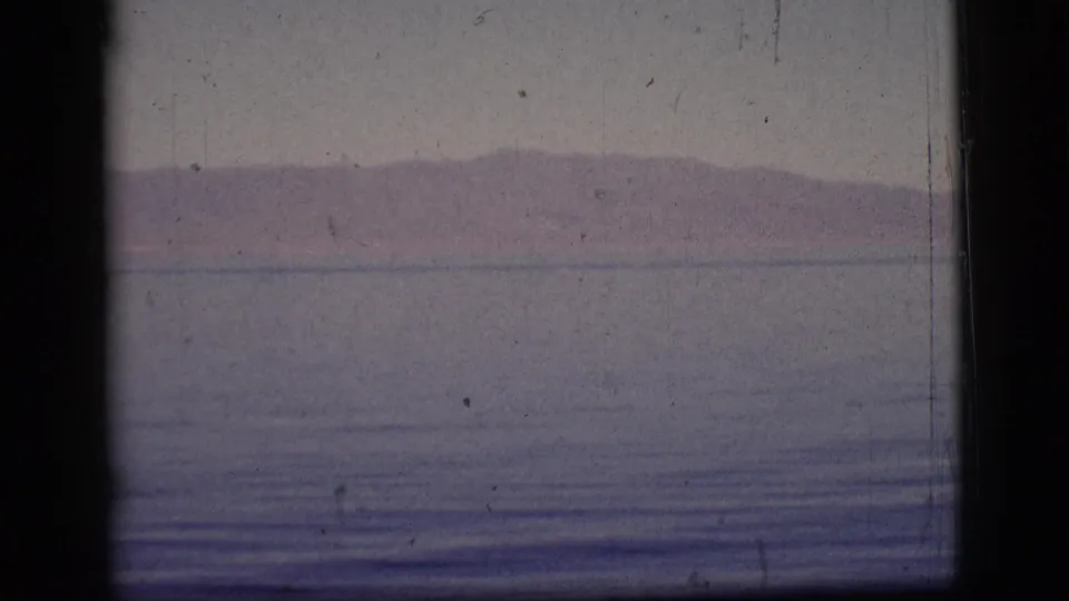 The 1961 8mm view holds on muted water, a far mountain horizon, hazy sky, and prominent dark film gate shading.