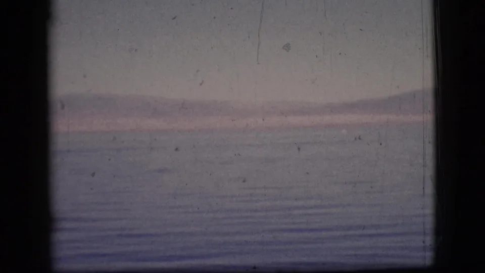 The final 1961 8mm frame holds on distant mountains across rippled water, with dark frame edges and visible archival film marks.