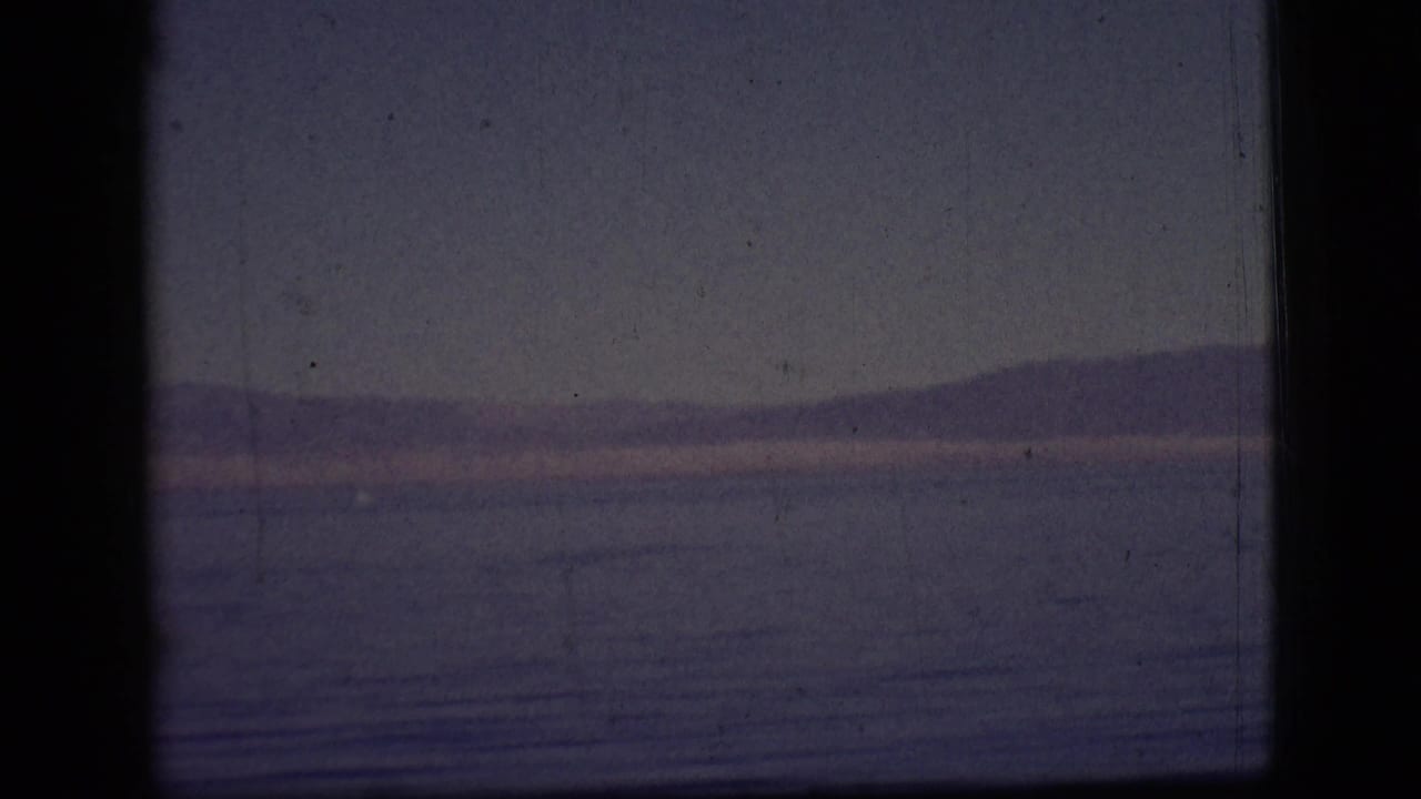 Calm water and distant low mountains under a muted purple sky, framed by dark film borders.