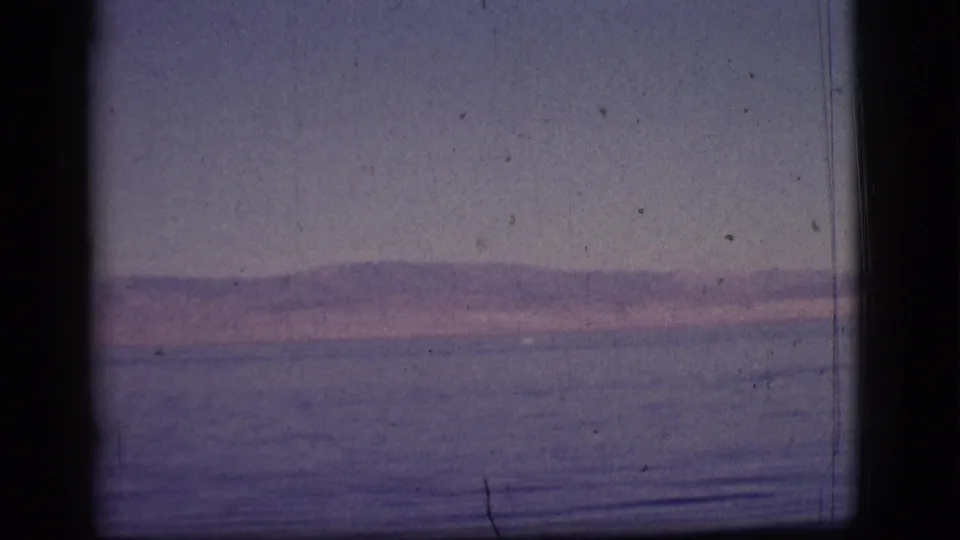 The 1961 home-movie view holds on water and a low mountain horizon, with grain and gate edges visible in the scan.