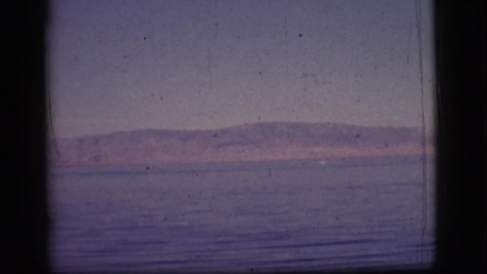 A late frame from the 8mm clip shows the same calm water and mountain vista, with visible dust and purple color cast.