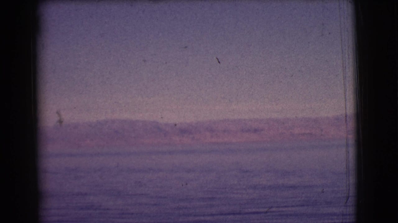Calm lake with distant hills under a pale purple sky, framed by dark 8mm film borders.