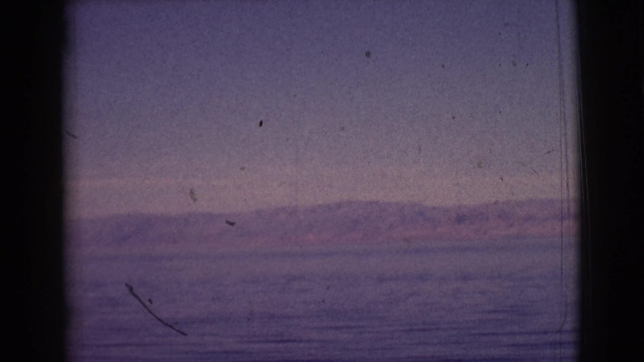 Calm lake and distant hills with visible film scratches and dark vertical frame edges.